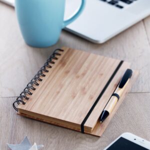 Notebook with logo BAMBLOC Bamboo notebook with logo twin-wire. 140 plain recycled paper pages (70 sheets). Matching push button ball pen with bamboo barrel and ABS details. Elastic pen holder. Depending on the surface we can use embroidery, engraving, 360° imprint or screen print.