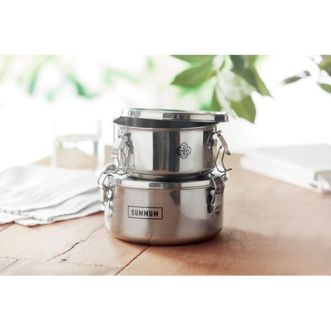 Gadget with logo Lunch boxes ELLES Stainless steel lunch boxes or storage set with logo with strong and secure side buckles. Capacity: 450 ml. and 900 ml. Bring your lunch with you to work or wherever you are with these two round shaped lunchboxes. The lunchbox has strong and secure side buckles to keep it leak proof. The food grade stainless steel will keep your food fresh. Available color: Matt Silver Dimensions: Ø14.5X7CM Height: 7 cm Diameter: 14.5 cm Volume: 2.65 cdm3 Gross Weight: 0.5 kg Net Weight: 0.396 kg Magnus Business Gifts is your partner for merchandising, gadgets or unique business gifts since 1967. Certified with Ecovadis gold!